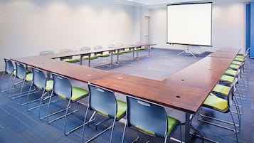 A conference room with a long table, chairs, and a projector screen.