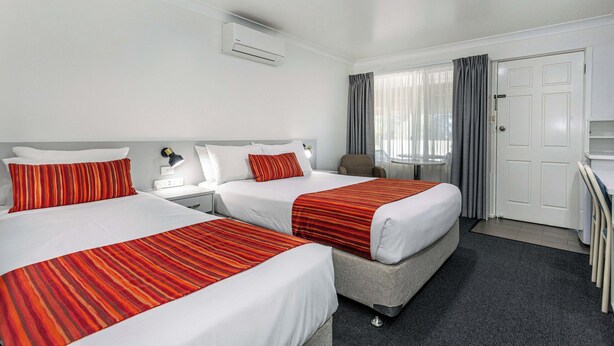 Une chambre d’hôtel avec deux lits, un bureau, une chaise, une porte et un appareil de climatisation.