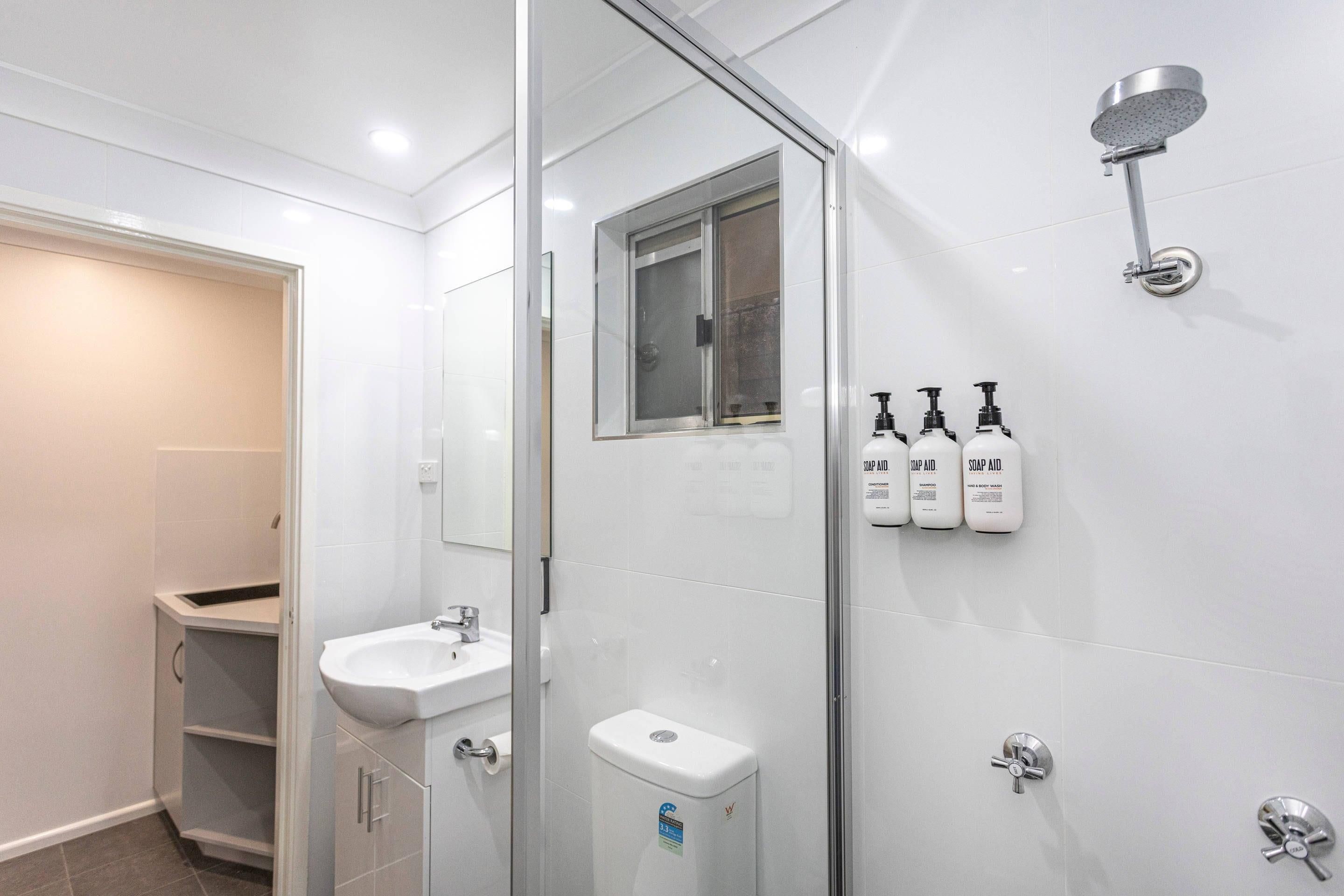 A modern bathroom with a glass shower enclosure, a sink, and three soap dispensers on the wall.