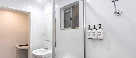 A modern bathroom with a glass shower enclosure, a sink, and three soap dispensers on the wall.