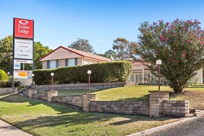 A motel with a signboard, a lawn, a brick wall, and a tree.