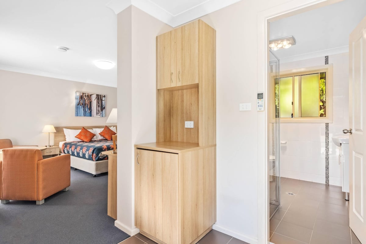 Ein Hotelzimmer mit einem Bett, einem Holzschrank, einem Korbstuhl und einem Badezimmer mit Duschkabine.