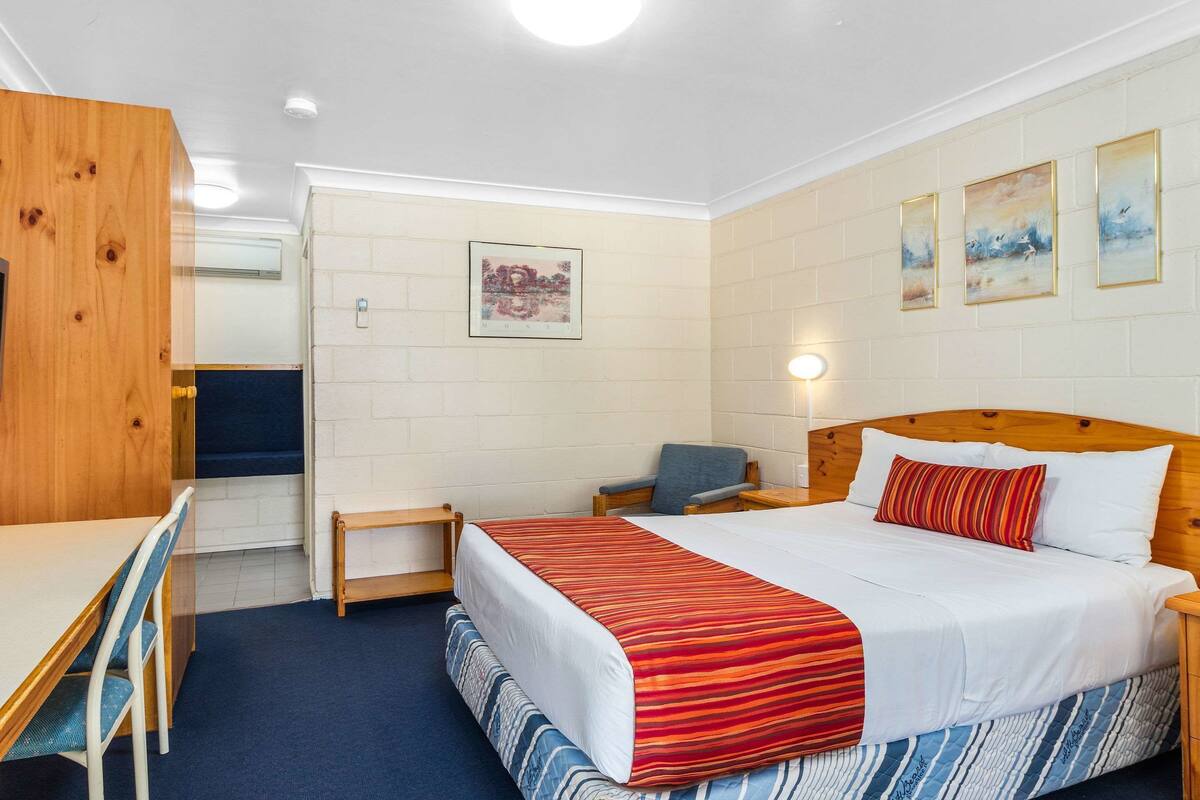 A hotel room with a bed, desk, chair, and artwork on the walls.