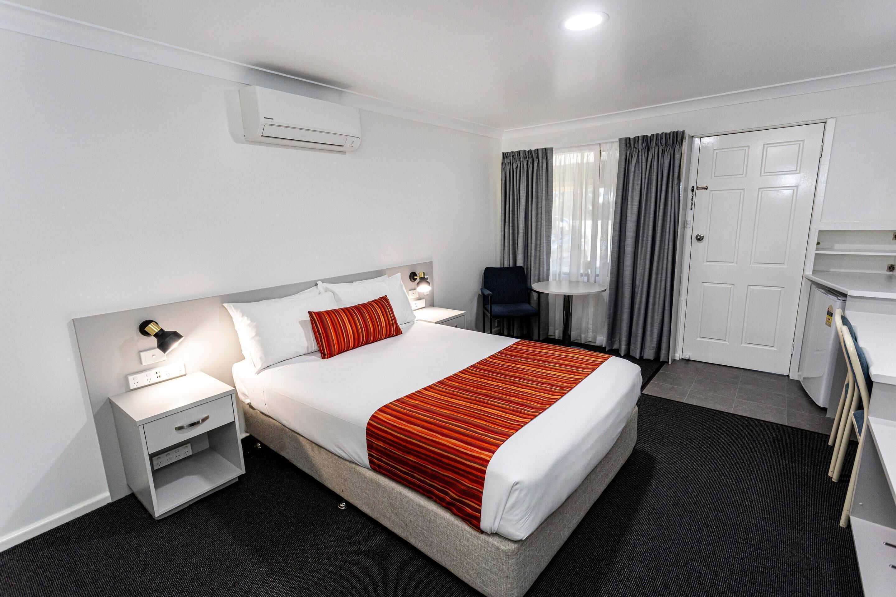 A hotel room with a bed, bedside tables, a desk, a chair, and a wardrobe.