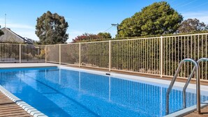 Une piscine rectangulaire entourée d’une clôture de sécurité en métal et bordée d’une terrasse dallée.