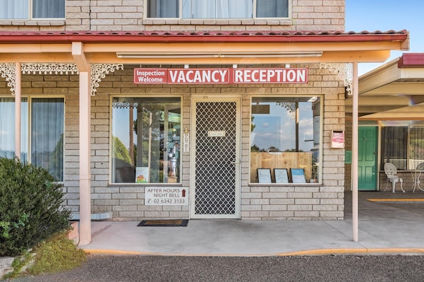 A building with a vacancy reception sign, a door with a security gate, and a small sign indicating after-hours night bell service. - Econo Lodge Alabaster (Cowra)