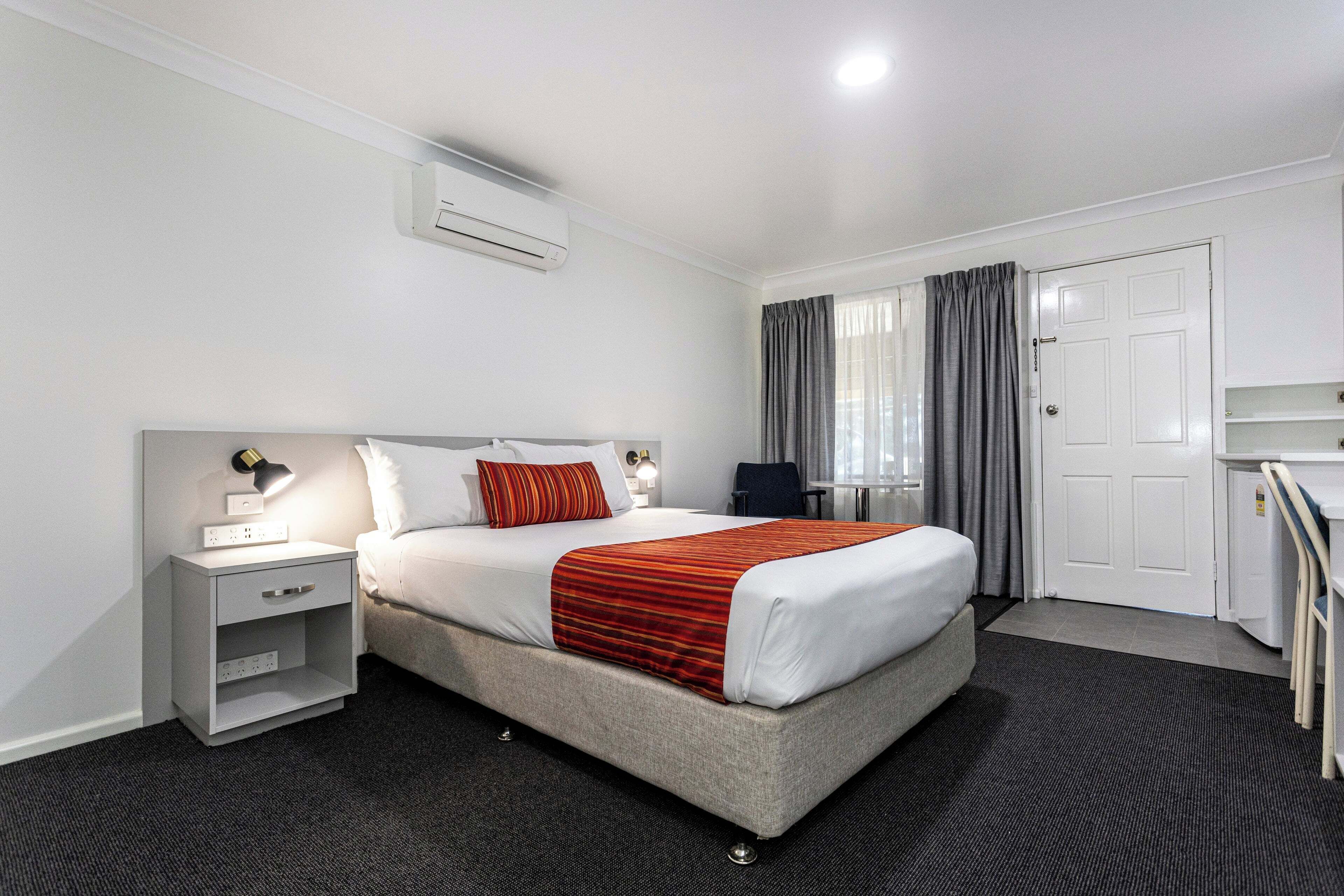 Una habitación de hotel con una cama, mesita de noche, lámpara y escritorio con una silla.