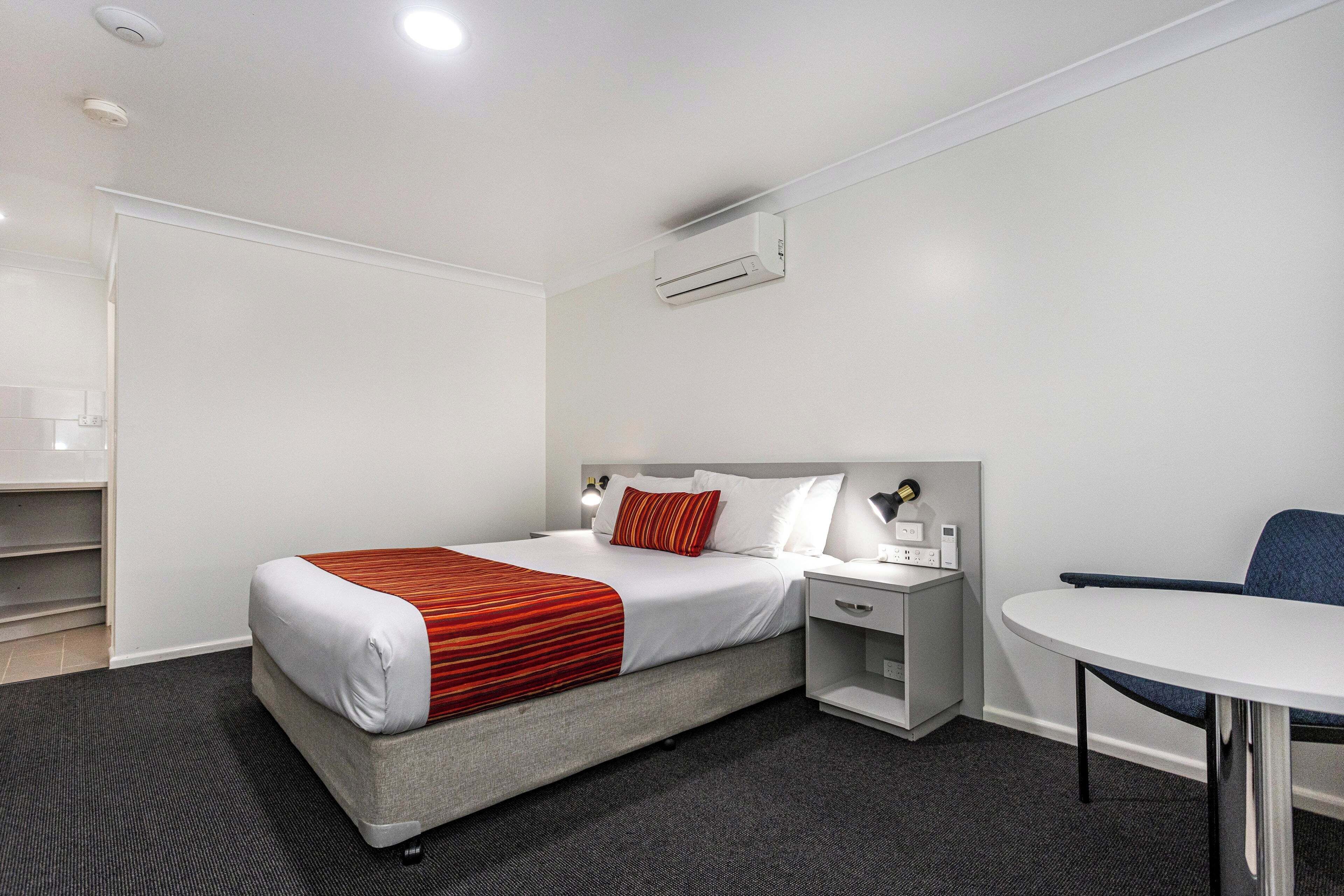Una habitación de hotel con cama, mesita de noche, silla y una pequeña mesa con lámpara.