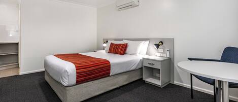 Una habitación de hotel con cama, mesita de noche, silla y una pequeña mesa con lámpara.