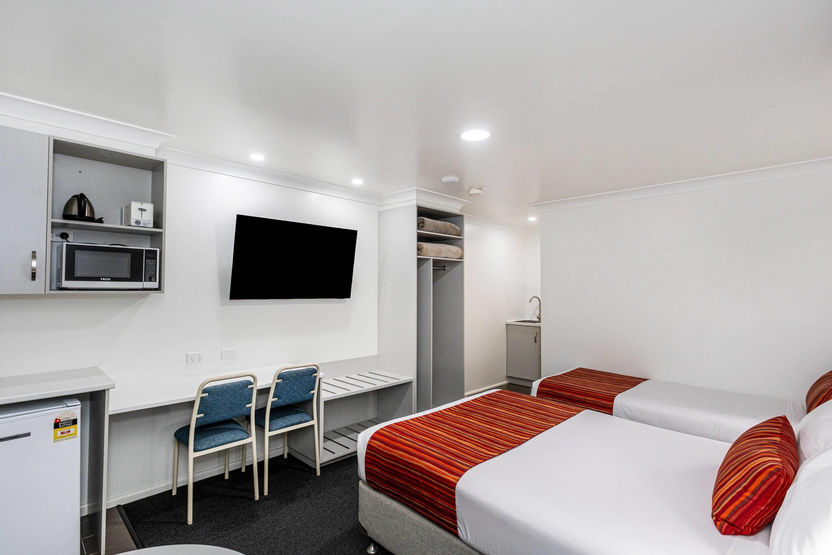 A hotel room with a bed, a desk, a chair, a TV, a microwave, and a wardrobe.