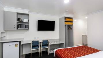A hotel room with a bed, desk, chairs, a TV, a mini-fridge, and a wardrobe.