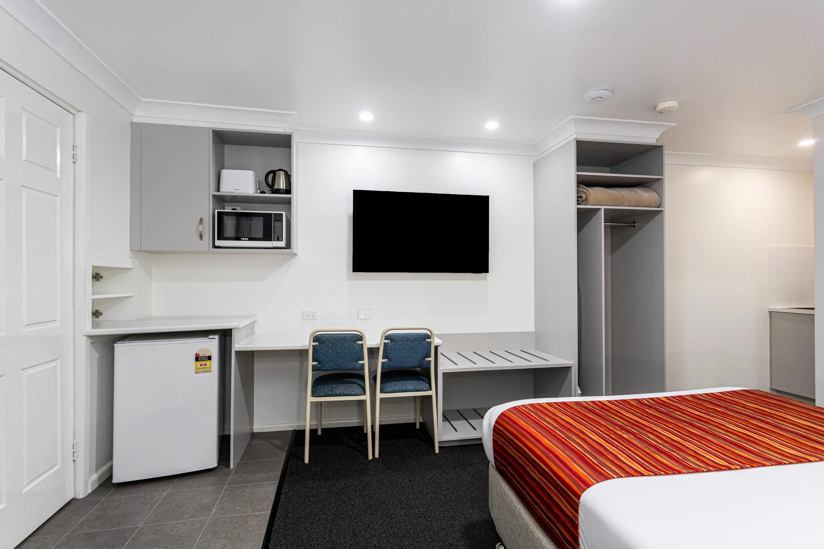Ein Hotelzimmer mit einem Bett, einem Schreibtisch mit zwei Stühlen, einem Fernseher, einer Minikühlschrank und einem Kleiderschrank.