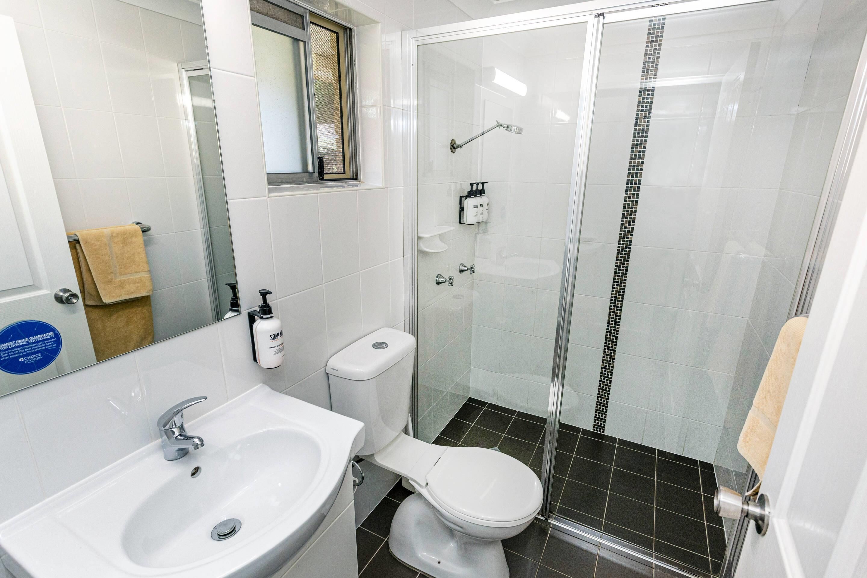 Une salle de bain avec un lavabo blanc, des toilettes et une douche fermée par des parois en verre.