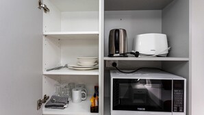 Une cuisine équipée d’un four à micro-ondes, d’une bouilloire et d’une théière, qui sont posés sur les étagères.