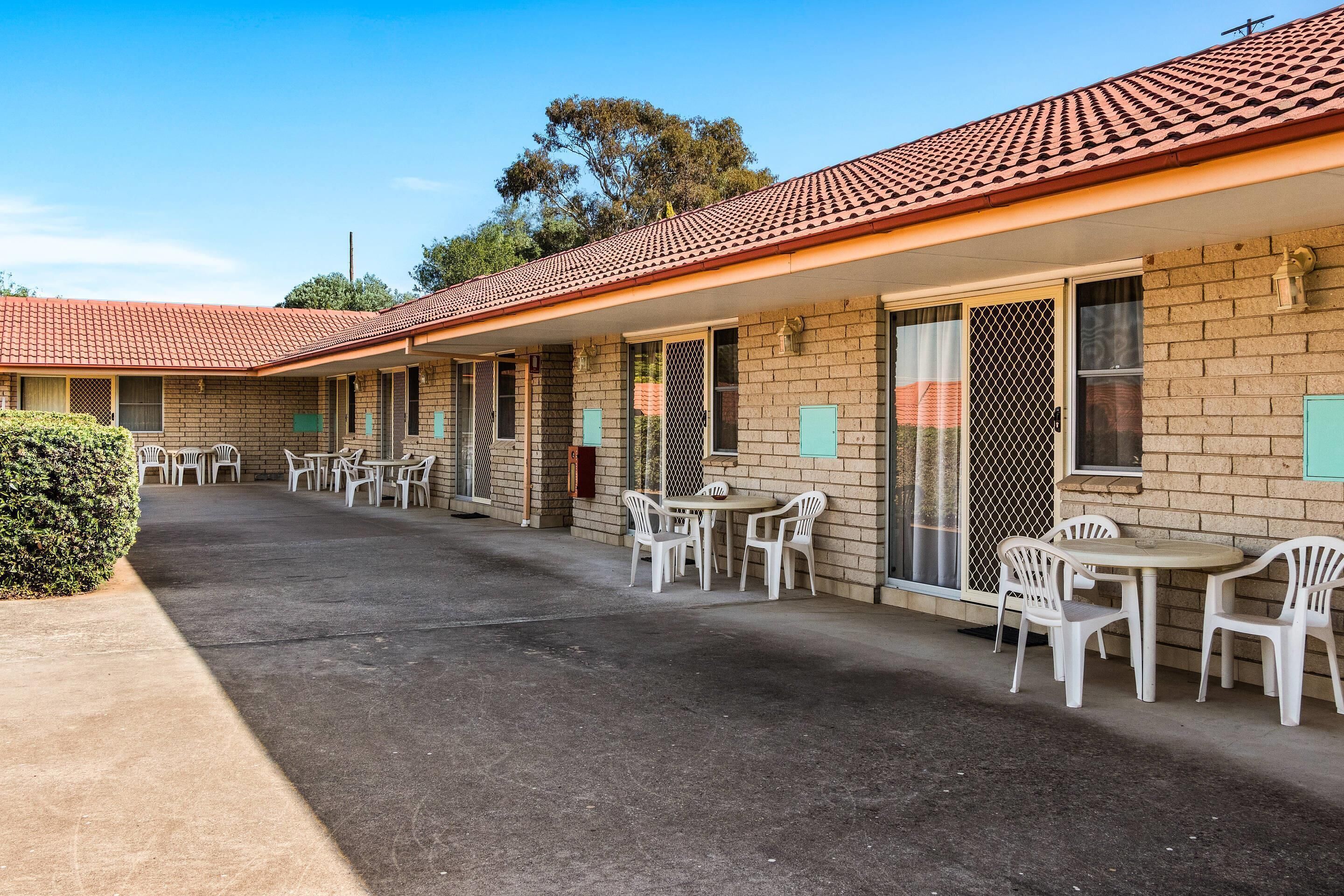 Un motel con varias habitaciones, asientos exteriores y un patio cubierto.