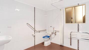 A bathroom with white tiled walls, a brown floor, a white toilet with a blue seat, a white sink, and a mirror above the sink.