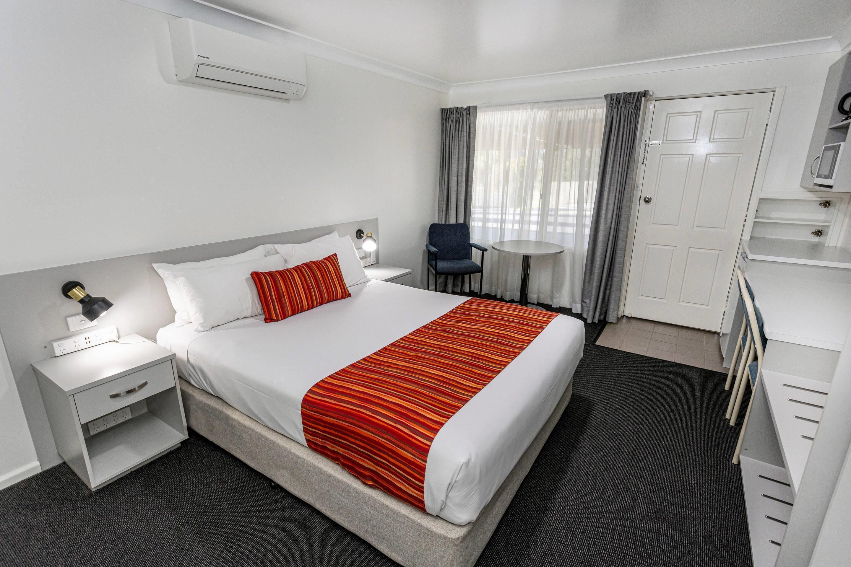 Una habitación de hotel con cama, mesita de noche, lámpara, silla, escritorio y armario.