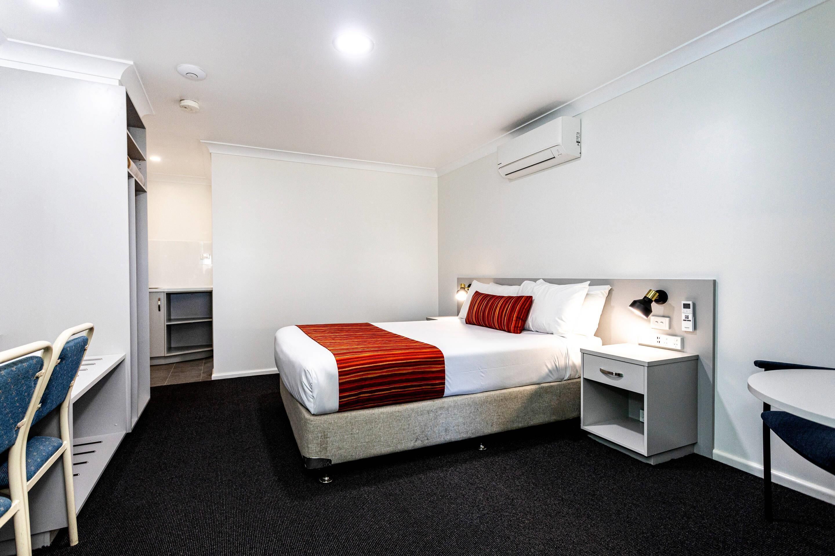 Ein Hotelzimmer mit Bett, Nachttisch, Stuhl, Schreibtisch und kleinem Tisch.