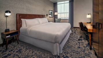 Ein Hotelzimmer mit einem großen Bett, einem Schreibtisch, einem Stuhl, einem Nachttisch und einem Fenster mit Vorhängen.