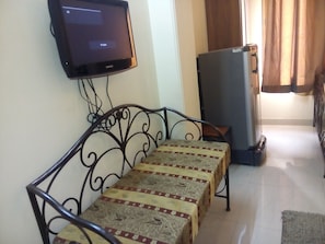 A living room with a sofa, a television mounted on the wall, and a refrigerator. - Hotel Pearl Plaza (New Delhi)