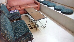 A living room with a brown sofa, a patterned blue sofa, a coffee table, and a shelf with blue cushions. - Hotel Pearl Plaza (New Delhi)