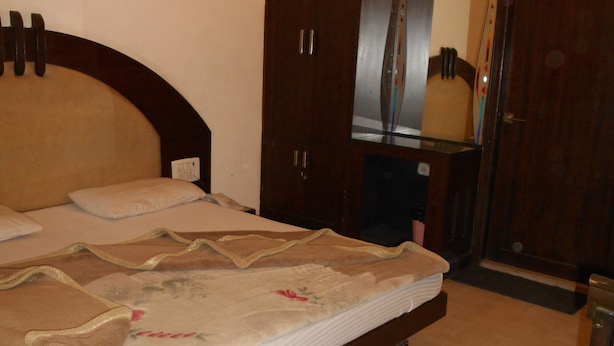 A bedroom with a wooden bed frame, a nightstand, a wardrobe, and a mirror. - Hotel Pearl Plaza (New Delhi)