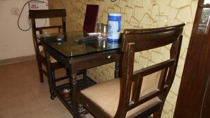 A dining area with a glass table, wooden chairs, a red book, a blue water dispenser, and a wall with a geometric pattern. - Hotel Pearl Plaza (New Delhi)