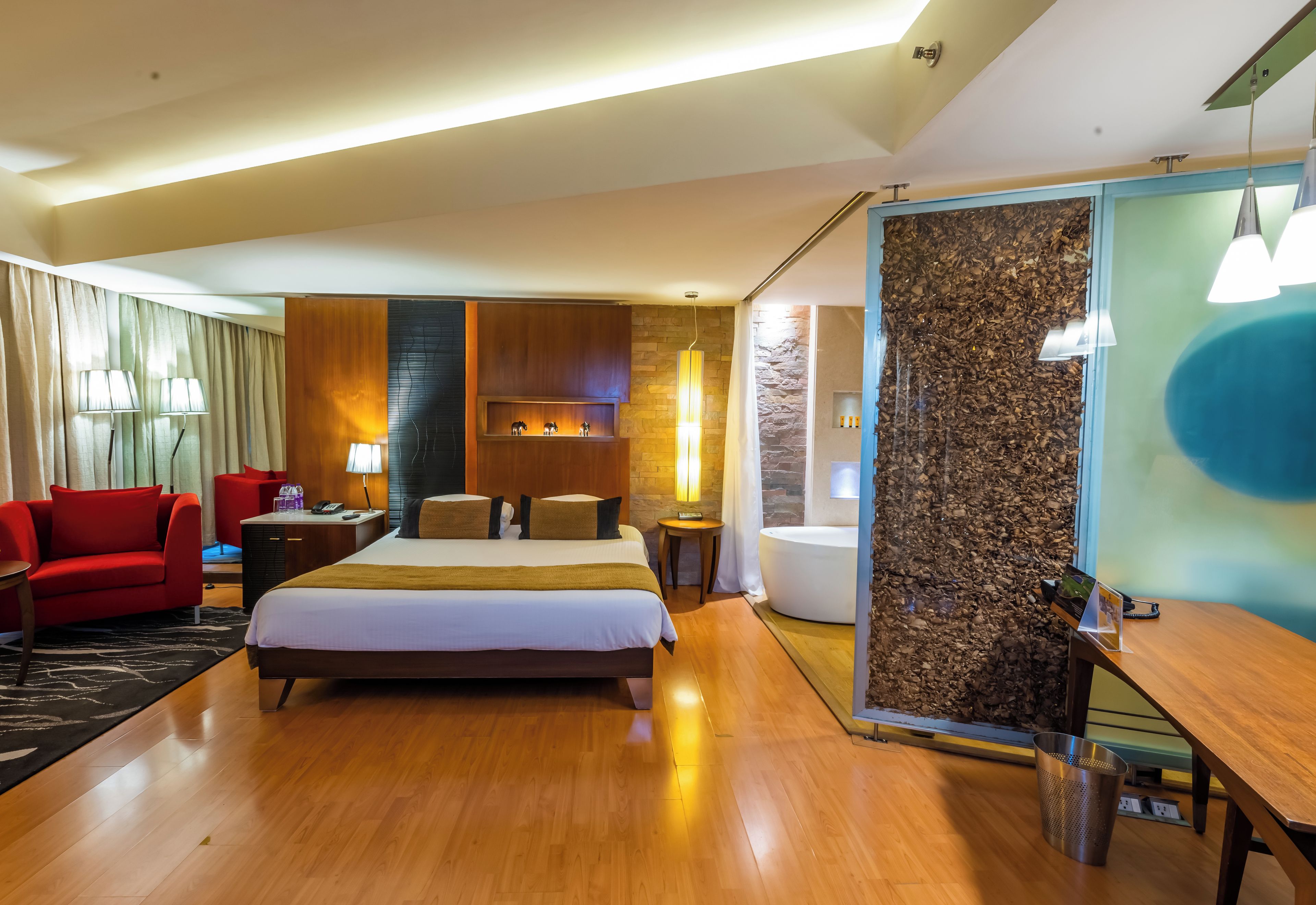 A hotel room with a large bed, a red armchair, a desk, and a shower area.