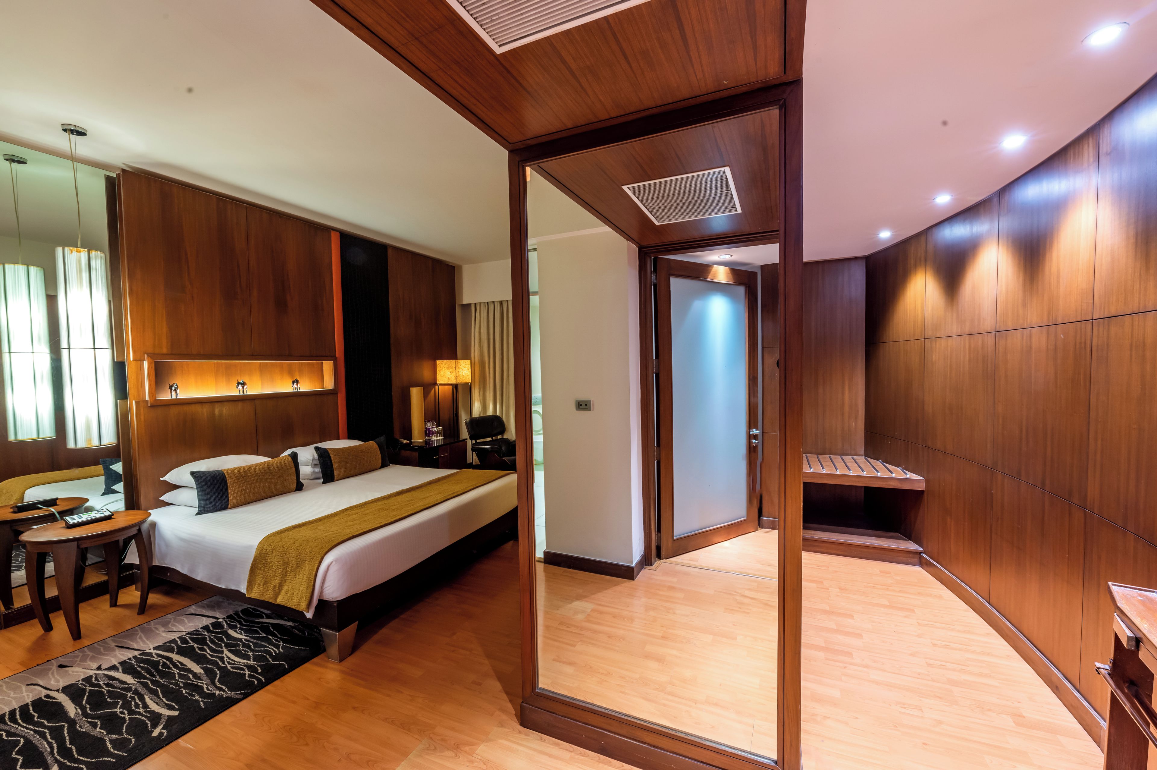 A hotel room with a large bed, bedside tables, a desk, a mirror, and a wardrobe.