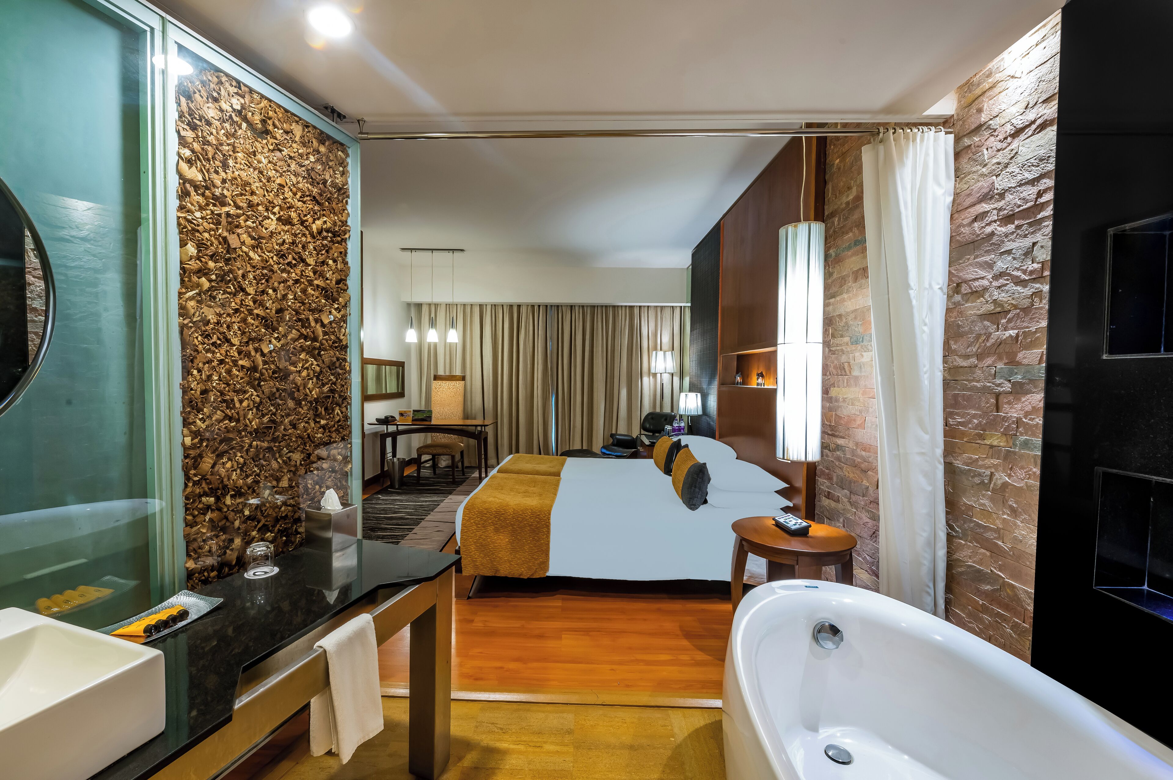A hotel room with a wooden wall, a large bed, a bathroom with a bathtub, and a desk with a lamp.