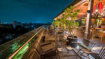 Una terraza en la azotea con mobiliario exterior, plantas en macetas y vistas de la ciudad de noche.