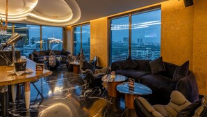 Ein stilvoller Lounge-Bereich mit Bar, Sitzgelegenheiten und großen Fenstern mit Blick auf die Stadt.