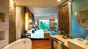 Ein modernes Hotelzimmer mit einem großen Bett, einer separaten Sitzecke, einer Badewanne und einem Badezimmer mit großem Spiegel und Waschbecken.