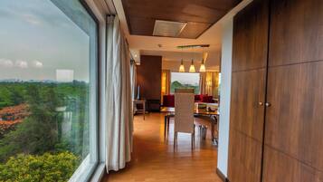 A modern interior with a wooden floor, a dining area with red chairs, and a view of greenery outside.