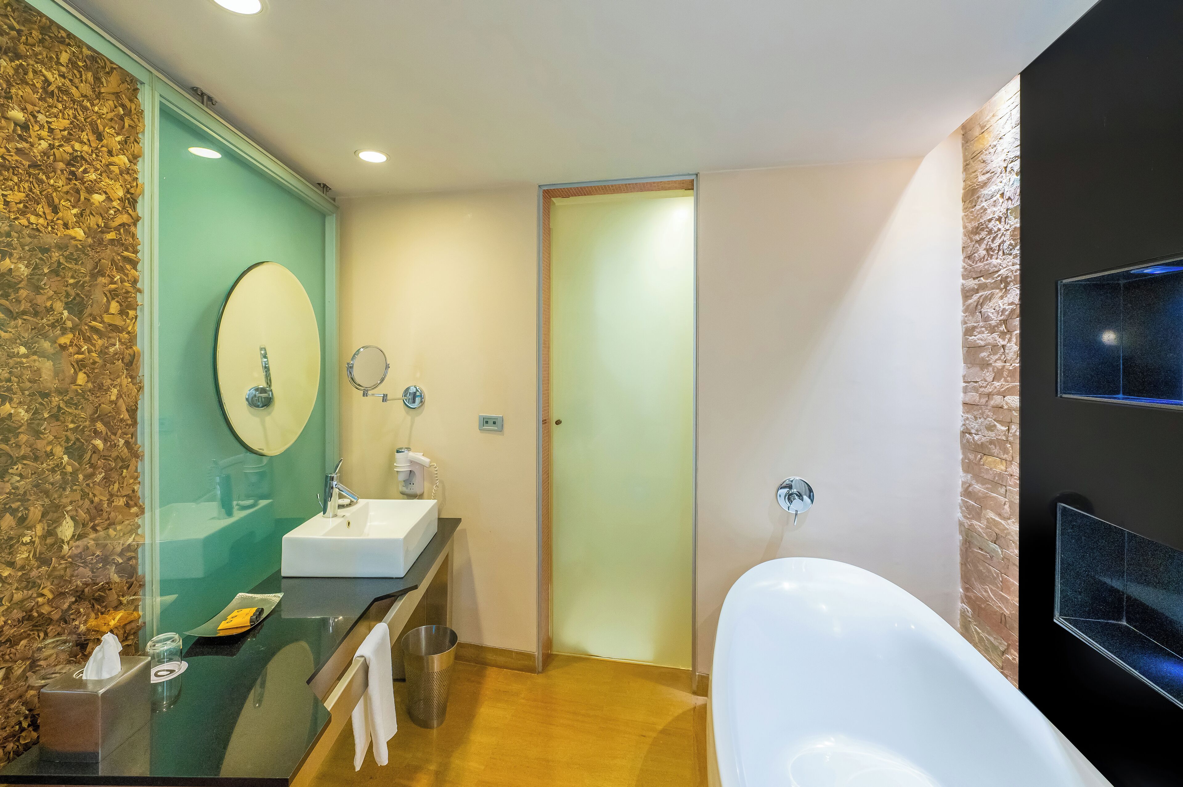 A modern bathroom with a large mirror, a white sink, a bathtub, and a wooden wall.