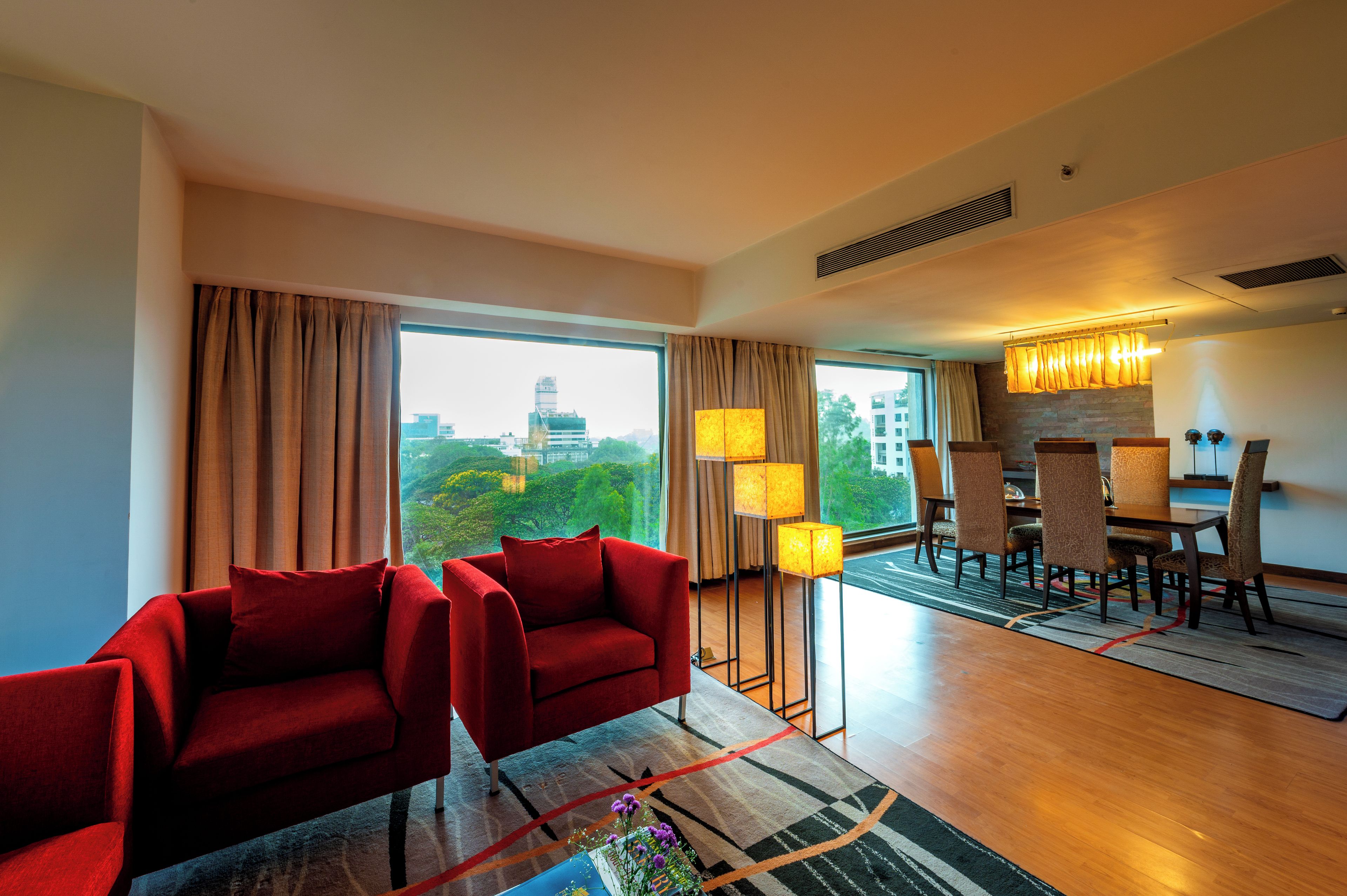 Une chambre d’hôtel avec une grande fenêtre, un coin repas et des canapés rouges.