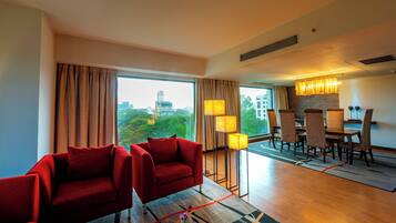 Une chambre d’hôtel avec une grande fenêtre, un coin repas et des canapés rouges.