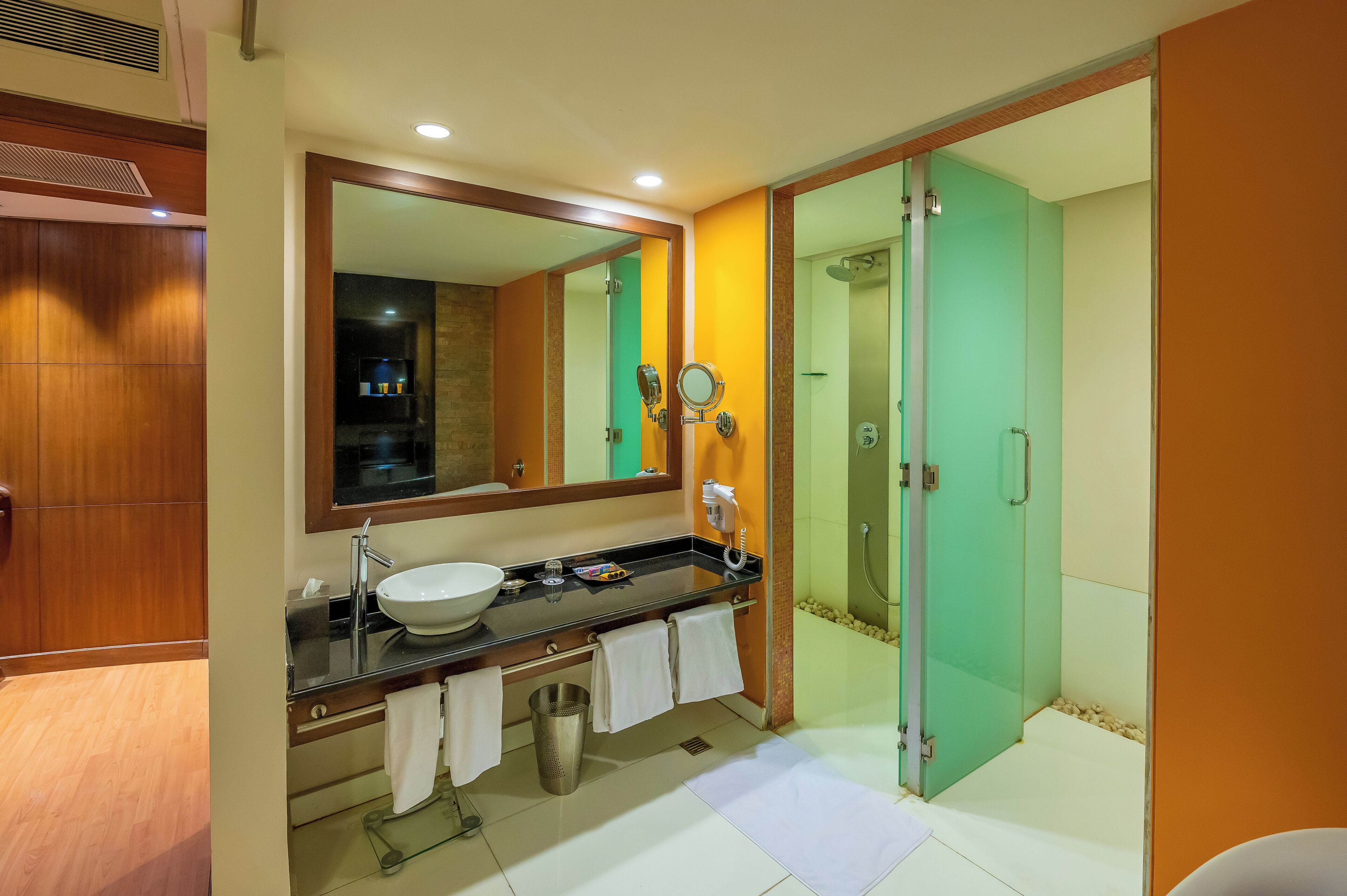 A modern bathroom with a large mirror, a sink, a towel rack, a trash can, and a glass-enclosed shower.