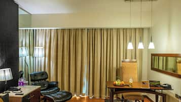 Une chambre d’hôtel comprenant un coin repas, un bureau avec un téléphone et une lampe, une chaise, ainsi qu’une table avec des fruits et un verre.