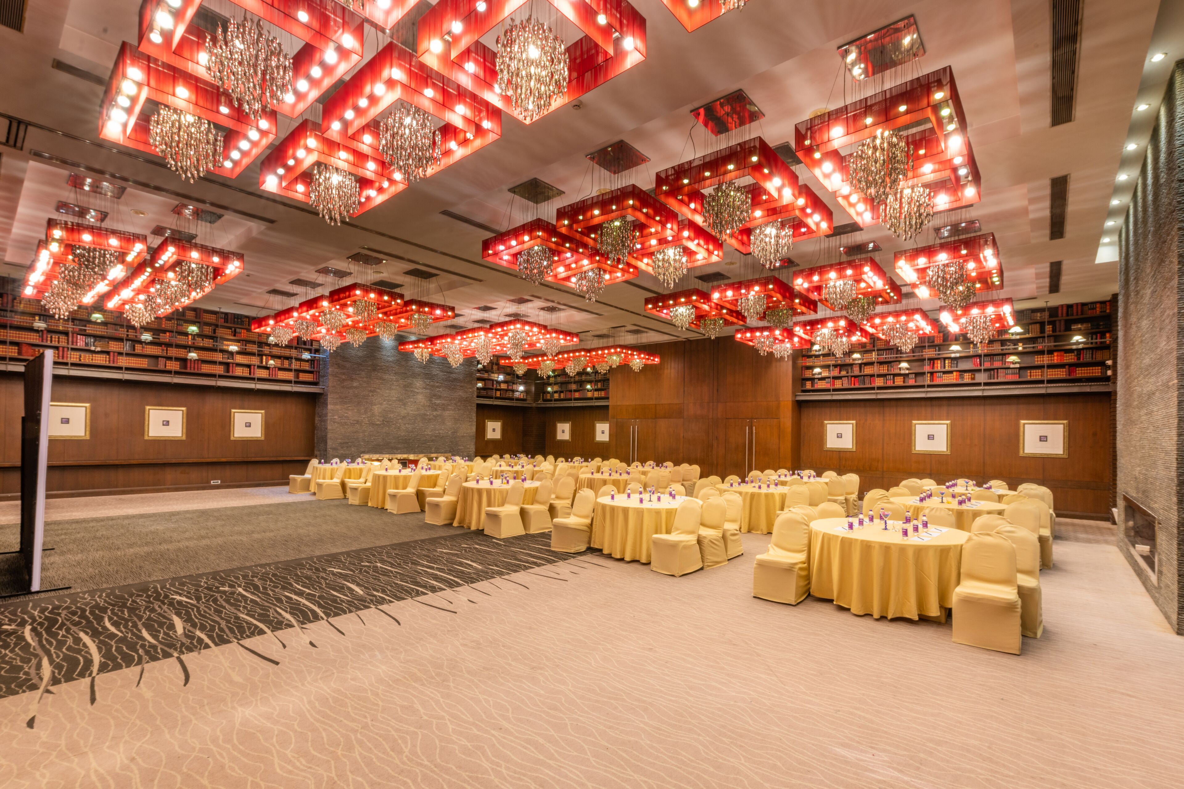 Un amplio salón de conferencias con mesas redondas, sillas amarillas y luces de techo rojas.
