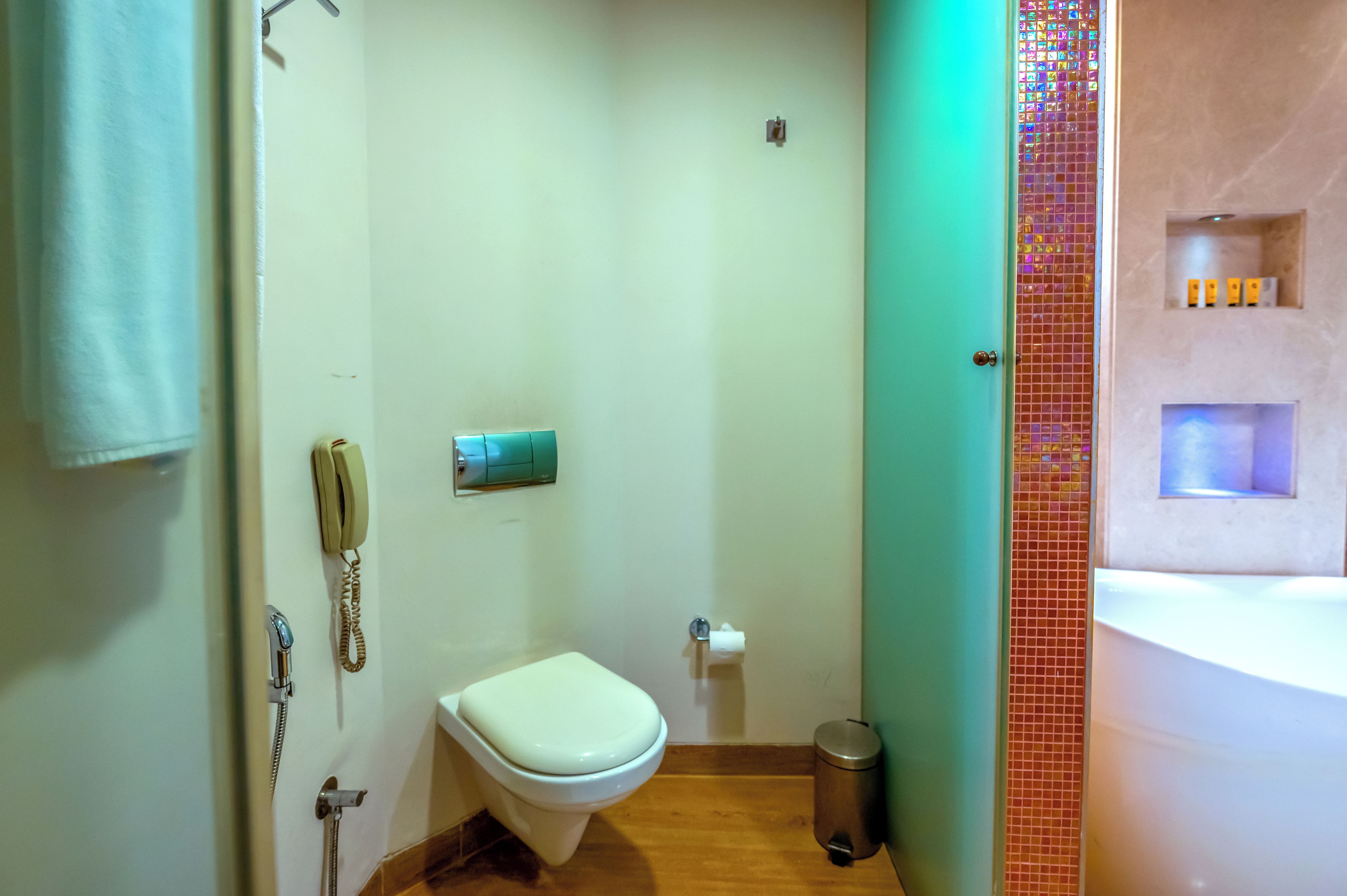 A small bathroom with a toilet, a hand dryer, a trash bin, and a wall-mounted telephone.