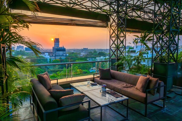A balcony with a sofa, coffee table, and potted plants. - O Hotel Pune (Pune)