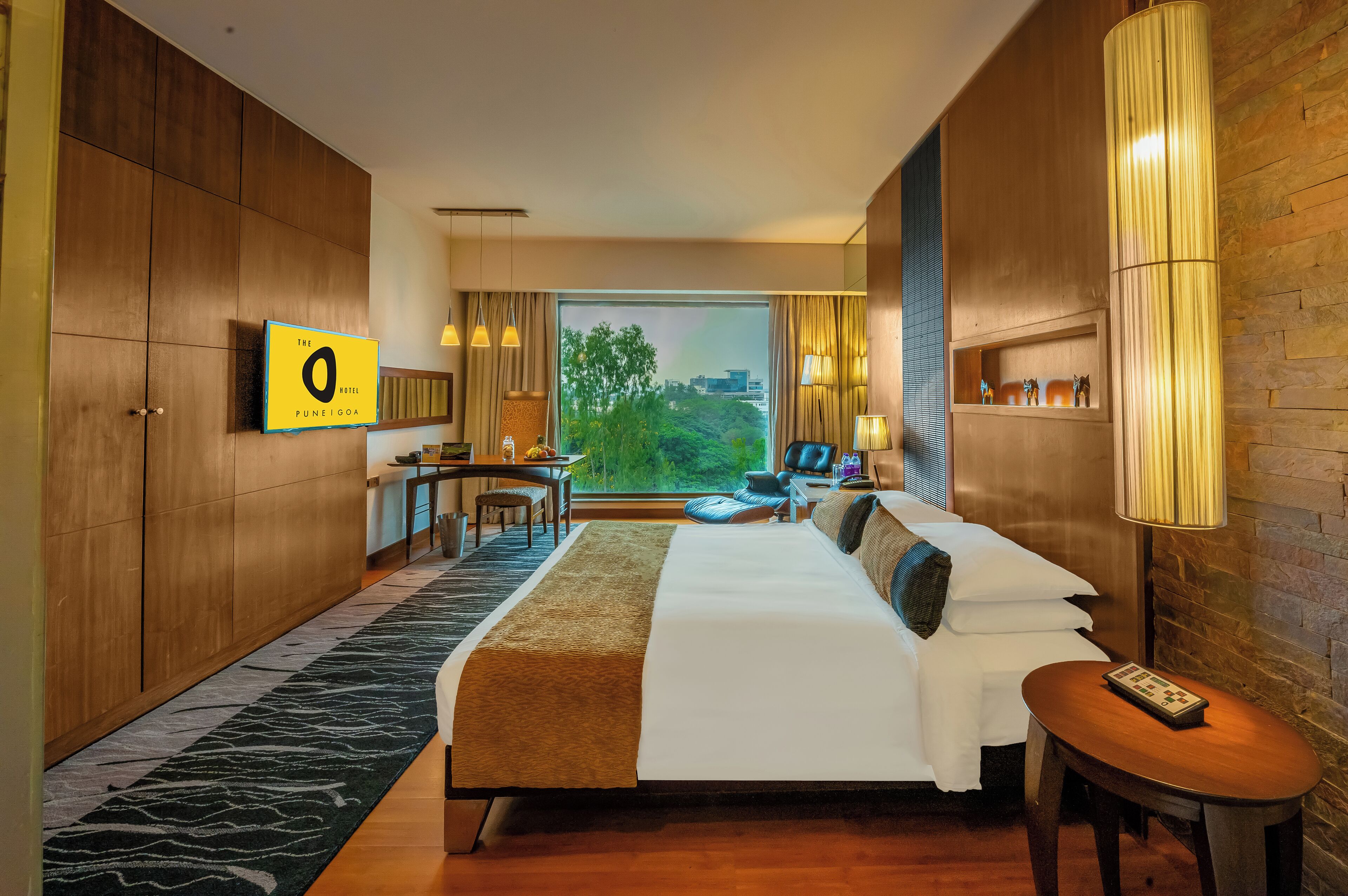 A hotel room with a large bed, a desk, a chair, a TV, and a view of the outdoors.
