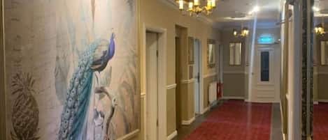 A hallway with a red carpet, a large peacock mural, and chandeliers.