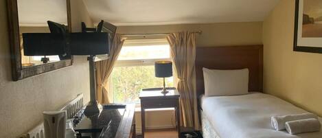 Habitación de hotel con cama, escritorio con lámpara, radiador y ventana con cortinas.