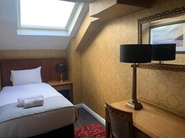 Una habitación de hotel con cama, mesita de noche, escritorio, lámpara y espejo.