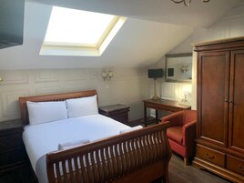 A bedroom with a skylight, a bed, a wooden chair, a desk, and a wardrobe.