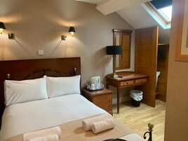 A hotel room with a bed, bedside table, lamp, and a view of a wooden closet.