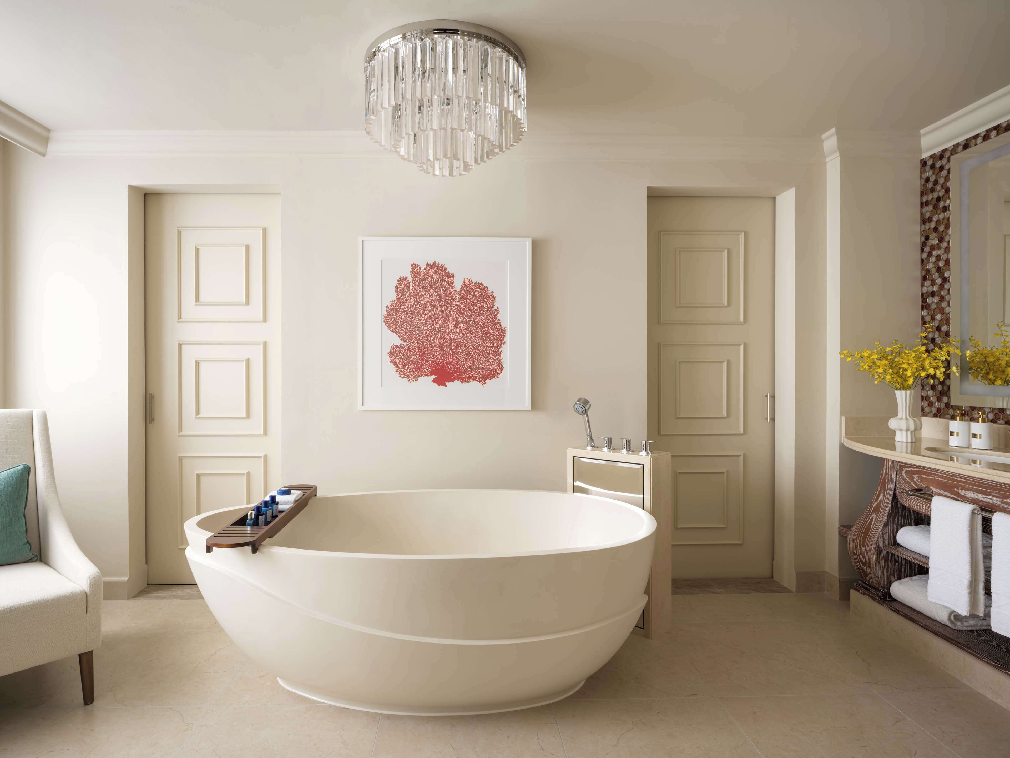 A modern bathroom with a freestanding bathtub, a large mirror, and a chandelier.