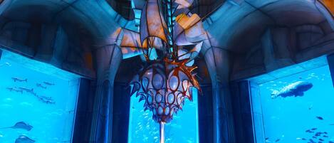 Un atrio con temática submarina, que presenta una escultura central, amplias paredes de acuario y un suelo de piedra.